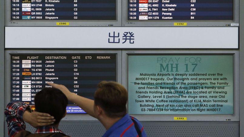Bystanders look at board displaying flight information and "Pray for MH17" message at Kuala Lumpur International Airport in Sepang